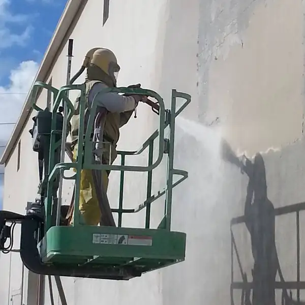 Sandblasting technician on a lift blasting a commercial building wall